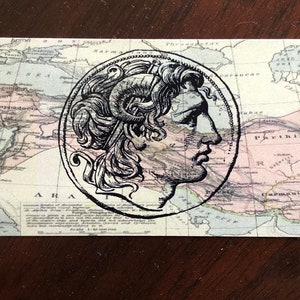 May include: A vintage map of the ancient world with a black and white illustration of a profile of a person's head in a circle in the center of the map.