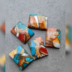 Pode incluir: Cinco cabochões retangulares de turquesa, vermelho, laranja e branco com manchas douradas. As pedras são cortadas e polidas para a fabricação de joias.