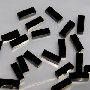 Könnte beinhalten: Eine Gruppe schwarzer rechteckiger Edelsteine, wahrscheinlich Obsidian, verstreut auf einer weißen Oberfläche. Die Edelsteine sind glatt und poliert, mit einem leichten Glanz.