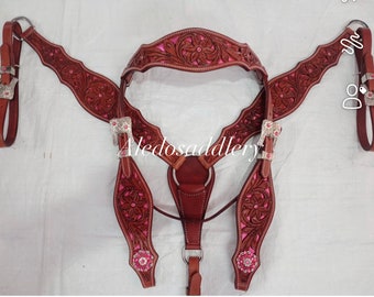 Puede incluir: Un conjunto de guarnicionería de caballo de cuero marrón con estampado floral rosa y hebillas plateadas. El conjunto incluye un pecho, una cabezada y dos riendas.