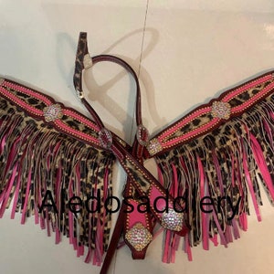 May include: A pink and brown leather horse bridle with fringe and rhinestones. The bridle is decorated with a leopard print pattern.