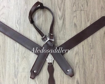 Puede incluir: Un petral de cuero marrón para caballos con herrajes metálicos plateados. El petral tiene una correa central con una placa decorativa plateada y el texto "Aledosaddlery". Las correas están conectadas con hebillas plateadas.