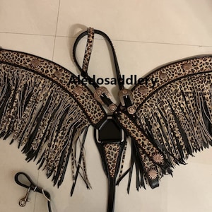 May include: A black leather horse halter with a leopard print design and fringe. The halter has a silver buckle and a brown leather strap.