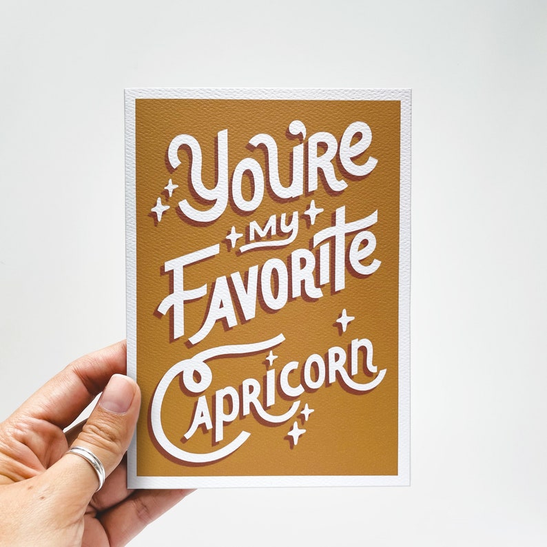May include: A mustard yellow card with white text that reads "You're my favourite Capricorn".