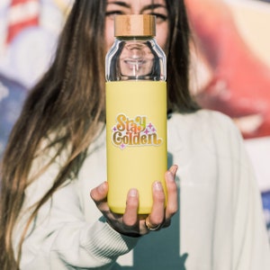 May include: A yellow reusable water bottle with a bamboo lid and a sticker that says "Stay Golden" in a rainbow gradient font.