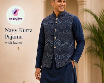 Può includere: Completo Kurta Pajama blu navy con giacca. L'immagine mostra un uomo che indossa un completo kurta pajama blu navy con un gilet fantasia con bottoni dorati. L'outfit è completato da mocassini in pelle marrone. Il testo "DesiGifts" è visibile.