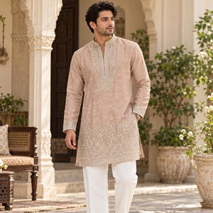 May include: A beige long-sleeved kurta featuring intricate silver embroidery around the mandarin collar, down the front placket, and along the hemline, paired with plain white trousers and brown leather loafers with a gold-tone metal detail.