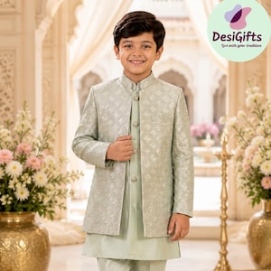 May include: A light sage green three-piece outfit consisting of a long-sleeved sherwani jacket with a subtle floral pattern, a matching solid-colored kurta underneath, and slim-fit trousers, paired with light beige slip-on shoes.