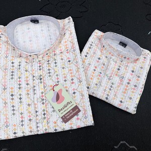 May include: Two white shirts with a colorful geometric pattern and a mandarin collar are displayed. One shirt is folded, and the other is open. A tag with the text "DesiGifts" is attached to the open shirt.
