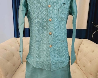 Può includere: Un set kurta pyjama blu turchese con un gilet a fantasia. Il gilet presenta un design geometrico e bottoni dorati. La kurta e il pyjama sono di un colore blu turchese solido.