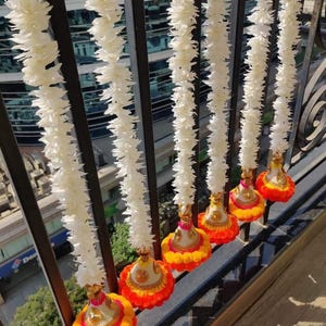 May include: White flower garlands with colorful tassels hanging from a railing. The tassels are made of orange, yellow, and pink fabric.