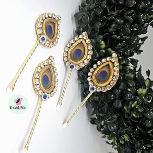 May include: Four decorative hair accessories with a peacock feather design. Each accessory features a gold-colored frame encrusted with clear rhinestones, surrounding a peacock feather. A small blue gem is at the base of each feather.