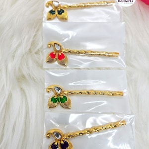 May include: Four gold hair pins with different colored stones. The stones are green, red, green, and purple. The hair pins are packaged in clear plastic bags. The text "Design - 1" is at the top of the image.