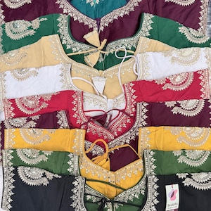 May include: A collection of embroidered blouses in various colors, including teal, burgundy, green, beige, white, red, yellow, and black. Each blouse features intricate silver-colored embroidery around the neckline and edges, with tie closures and a tag that says "Desigifts".