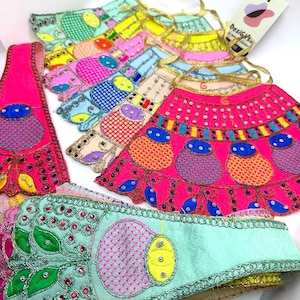 May include: A set of colorful fabric skirts with embroidered floral designs and gold trim. The skirts are layered and feature different patterns and colors, including pink, blue, yellow, and green. The skirts are decorated with sequins and beads.
