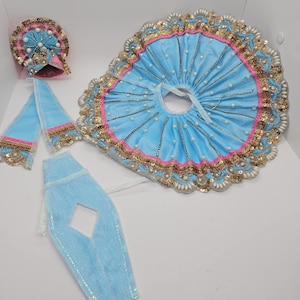 May include: A blue and gold baby outfit with a skirt, pants, and a hat. The outfit is decorated with sequins, pearls, and lace.