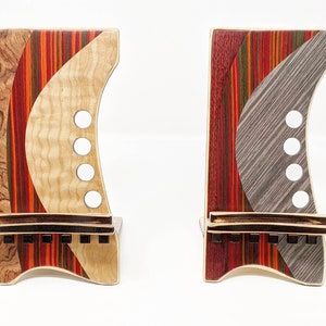 May include: Two wooden phone stands with a unique, colourful and abstract design. The stands are made of different types of wood, including maple, cherry and walnut. The stands are both approximately 15 cm tall and 10 cm wide.