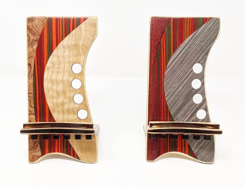 May include: Two wooden phone stands with a unique, colourful and abstract design. The stands are made of different types of wood, including maple, cherry and walnut. The stands are both approximately 15 cm tall and 10 cm wide.