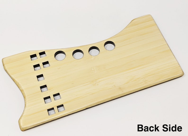 May include: A light brown wooden tool with a curved top and a flat bottom. The tool has several round holes and square holes cut out of it. The back side of the tool is shown in the image.