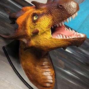 Può includere: Una scultura di testa di drago gialla e marrone con la bocca aperta e denti affilati. La scultura è montata su una base in legno nero.