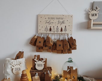 May include: A wooden advent calendar with 24 small houses, each with a small door. The calendar is decorated with a sign that says "Kalendarz Adwentowy Tadzia i Steffi". There are also two wooden reindeer ornaments with the names "Tadzio" and "Steffcia" on them.