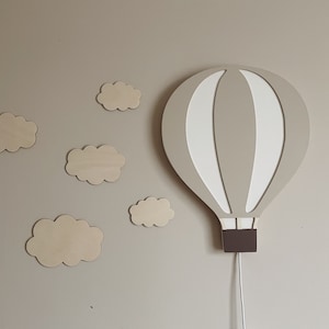 May include: A light brown wooden hot air balloon wall decor with white stripes and a brown base. The balloon is hanging from a white cord. There are five small wooden clouds on the wall behind the balloon.