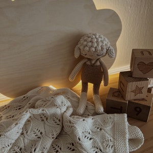 May include: A white crocheted blanket with a delicate pattern, a crocheted lamb toy, and wooden blocks with numbers and a star design.