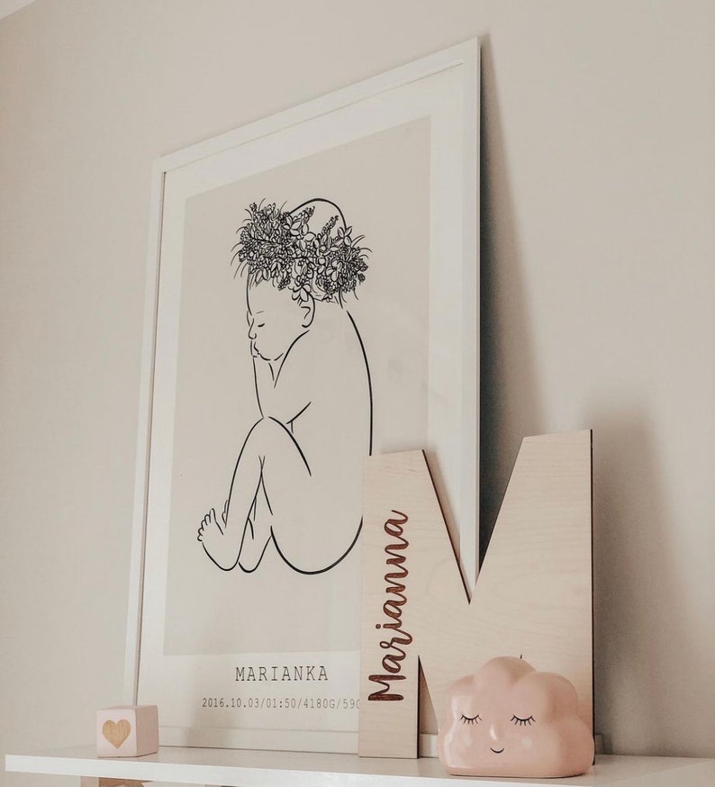 Pu&ograve; includere: Un disegno in bianco e nero di un bambino con una corona di fiori. Il disegno &egrave; su uno sfondo beige. La cornice &egrave; bianca. Il nome "Marianka" e la data "2016.10.03/01:50/4180G/59" sono stampati sotto il disegno. Una lettera in legno "M" con il nome "Marianna" inciso su di essa &egrave; appoggiata contro la cornice. Un oggetto rosa a forma di nuvola con un viso sorridente &egrave; davanti alla lettera. Un piccolo blocco di legno a forma di cuore &egrave; sullo scaffale sotto la cornice.