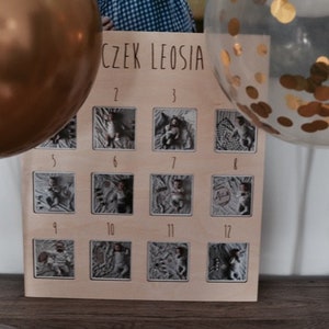 Może przedstawiać: Drewniana tablica z 12 oprawionymi zdjęciami dziecka. Tablica ma napis "CZĘK LEOSIA" u g&oacute;ry i numery od 1 do 12 pod zdjęciami.