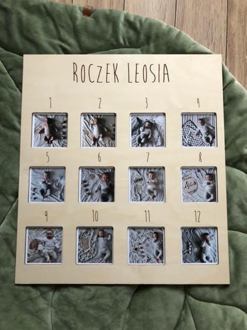 Może przedstawiać: Drewniana ramka na zdjęcia z 12 indywidualnymi ramkami na zdjęcia, każda z numerem od 1 do 12. Ramka ma napis "Roczek Leosia" u g&oacute;ry.