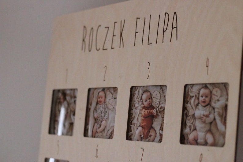 Może przedstawiać: Drewniany panel do wyświetlania zdjęć z napisem "ROCZEK FILIPA" na g&oacute;rze. Panel ma osiem kwadratowych otwor&oacute;w na zdjęcia, ponumerowanych od 1 do 8. Otwory są wypełnione zdjęciami małego chłopca w r&oacute;żnym wieku.