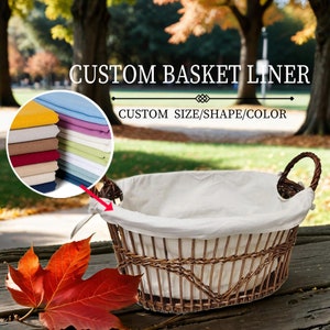 以下が含まれることがあります： 2つのハンドルが付いた籐のバスケットの中に、白い布製のバスケットライナーが入っています。バスケットライナーは、バスケットに合わせてサイズと形がカスタマイズされています。バスケットの上には、「CUSTOM BASKET LINER」と「CUSTOM SIZE/SHAPE/COLOR」のテキストが表示されています。画像の左上隅には、さまざまな色の布のサンプルが積み重ねられています。