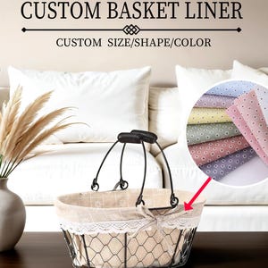 Könnte beinhalten: Ein schwarzer Drahtkorb mit einem individuellen Stofffutter. Das Futter ist beige mit einer weißen Spitzenborte und einem Blumenmuster. Der Text "CUSTOM BASKET LINER" und "CUSTOM SIZE/SHAPE/COLOR" ist im Bild sichtbar.