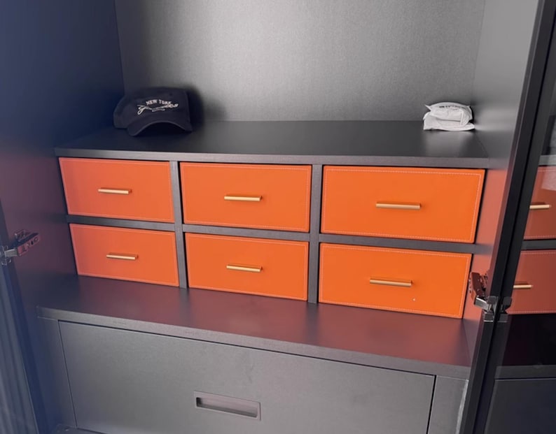 May include: A black cabinet with six orange drawers and a black drawer below. The cabinet has a black top with a black baseball cap with the text "NEW YORK" on it.