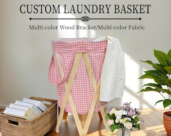 Puede incluir: Una cesta de ropa de gingham rosa y blanco con un marco de madera. La cesta está de pie sobre un suelo de madera. La cesta está hecha de tela y tiene un marco de madera. La cesta está sentada sobre un suelo de madera.