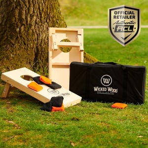 Może przedstawiać: Drewniany zestaw cornhole z czarną torbą transportową. Zestaw zawiera dwie plansze do cornhole, osiem woreczków z fasolą i torbę transportową z logo Wicked Wood. Plansze są wykonane z drewna i mają naturalne wykończenie. Woreczki z fasolą są wykonane z płótna i mają czarno-pomarańczowy wzór. Torba transportowa jest wykonana z czarnego płótna i ma zamek błyskawiczny.
