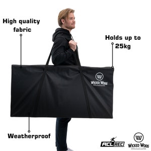 Könnte beinhalten: Eine schwarze, wetterfeste Tragetasche mit einem schwarzen Riemen und dem Text "Wicked Wood" in Weiß. Die Tasche wird von einer Person gehalten. Der Text "Holds up to 25kg" steht über der Tasche. Der Text "High quality fabric" steht über dem Kopf der Person. Der Text "Weatherproof" steht unter der Tasche.