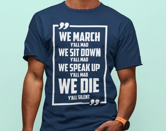 Puede incluir: Una camiseta azul marino con un estampado gráfico blanco que dice "WE MARCH Y'ALL MAD WE SIT DOWN Y'ALL MAD WE SPEAK UP Y'ALL MAD WE DIE Y'ALL SILENT" en un cuadro blanco con comillas.