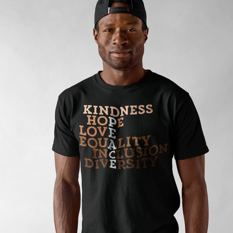 May include: A black t-shirt with the words "KINDNESS", "HOPE", "LOVE", "PEACE", "EQUALITY", "INCLUSION", and "DIVERSITY" printed in brown and white.
