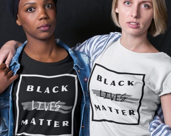 May include: Two people wearing t-shirts with the text "Black Lives Matter" printed in a white box with a black border. The text is stylized with a gray brushstroke effect. One person is wearing a black t-shirt and the other is wearing a white t-shirt.