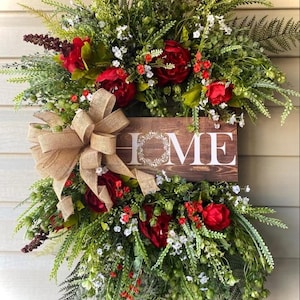 May include: A green and red floral wreath with a wooden sign that says "HOME" in white letters. The wreath is decorated with a burlap bow.