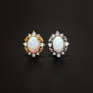 May include: Two opal stud earrings. One earring has a gold-coloured setting with a filigree design and small clear stones. The other earring has a silver-coloured setting with a similar design. Both earrings have an oval-shaped opal centre stone.