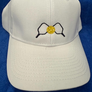 May include: A white baseball cap with a curved brim. The cap features a yellow and black embroidered design on the front. The cap is made of a durable fabric and has a structured fit.
