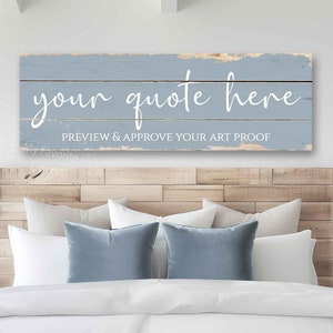 May include: A rectangular, light blue wooden sign with the text "your quote here" in white script. Below, the text reads "PREVIEW & APPROVE YOUR ART PROOF". The sign is mounted above a bed with white bedding and blue pillows.