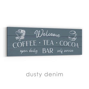 May include: A rectangular sign with a dusty denim background features the words "Welcome" and "COFFEE &bull; TEA &bull; COCOA" in white script. The sign also includes the phrases "open daily," "BAR," and "self service." White line drawings of coffee cups are on each side.