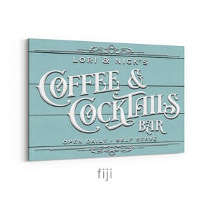 May include: A rectangular sign with a light blue background and white lettering. The sign reads "LORI & NICK'S COFFEE & COCKTAILS BAR" with the words "OPEN DAILY - SELF SERVE" below. Decorative flourishes are at the top and bottom.