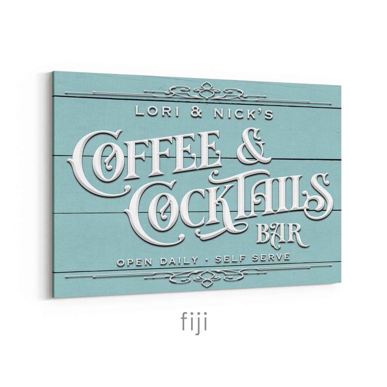 May include: A rectangular sign with a light blue background and white lettering. The sign reads "LORI & NICK'S COFFEE & COCKTAILS BAR" with the words "OPEN DAILY - SELF SERVE" below. Decorative flourishes are at the top and bottom.