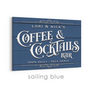 May include: A rectangular sign with a blue background and white lettering. The sign reads "LORI & NICK'S COFFEE & COCKTAILS BAR" with the words "OPEN DAILY - SELF SERVE" below. The sign is labeled "sailing blue".