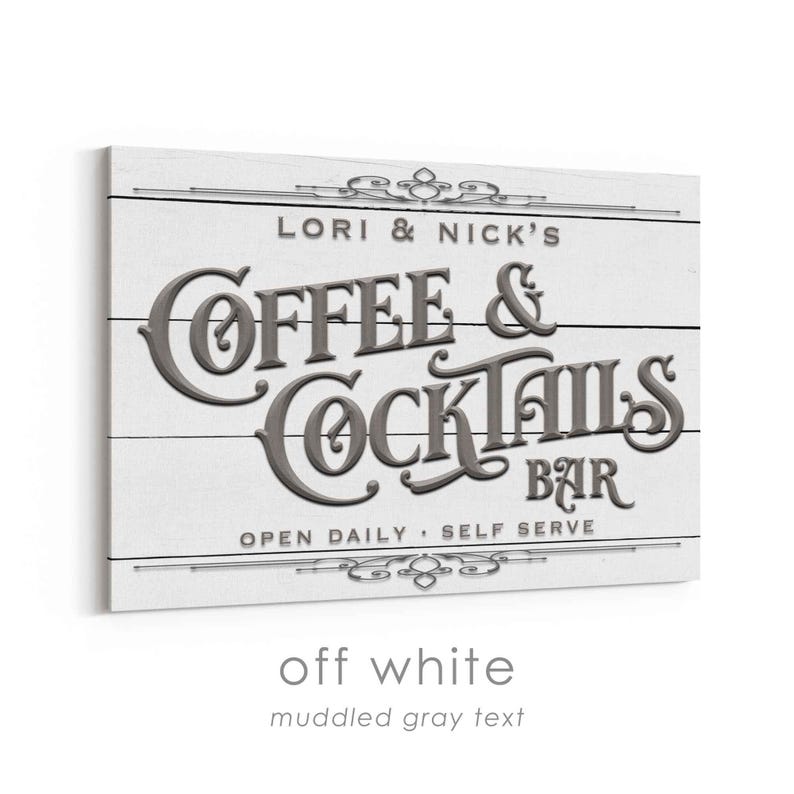 May include: Off-white wooden sign with the text "LORI & NICK'S COFFEE & COCKTAILS BAR" in muddled gray. The sign also includes the phrases "OPEN DAILY" and "SELF SERVE". Decorative flourishes are at the top and bottom.