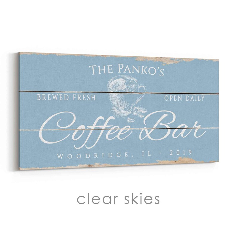 Pode incluir: Uma placa de madeira azul clara com texto branco que diz "The Panko's Coffee Bar" com um gr&aacute;fico de x&iacute;cara de caf&eacute;. O texto adicional inclui "Brewed Fresh", "Open Daily" e "Woodridge, IL 2019". A placa tem um aspeto envelhecido.
